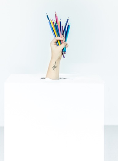 arm sticking out of a white box holding lots of coloured pencils